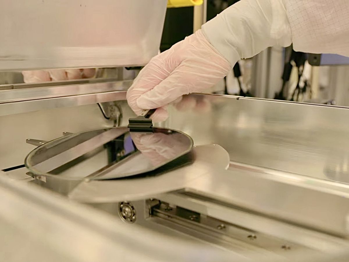 A gloved hand lifting a wafer out of processing equipment with tweezers